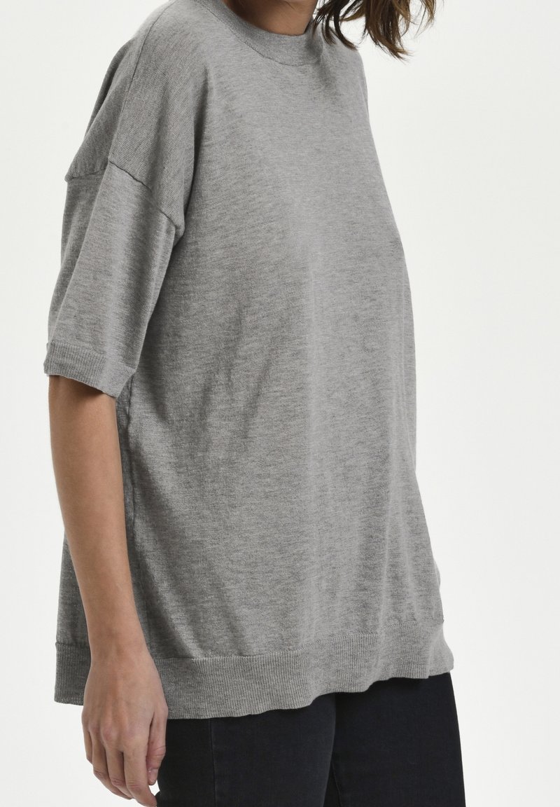 Lys grå strikket bluse med rund hals, drop-skulder og ribbede kanter. Stoffet ser blødt og let tekstureret ud.