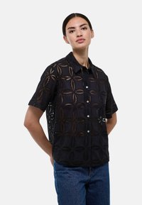 Chemise noire à manches courtes avec un motif floral découpé, fermeture à boutons et col. Tissu léger au toucher texturé.