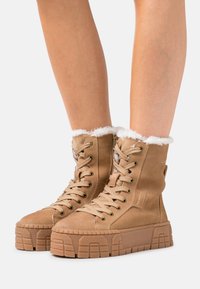 Hellbraune Ankle Boots aus Wildleder mit einem flauschigen weißen Kunstfellkragen, dicker Plateausohle und detailliertem Schnürverschluss.
