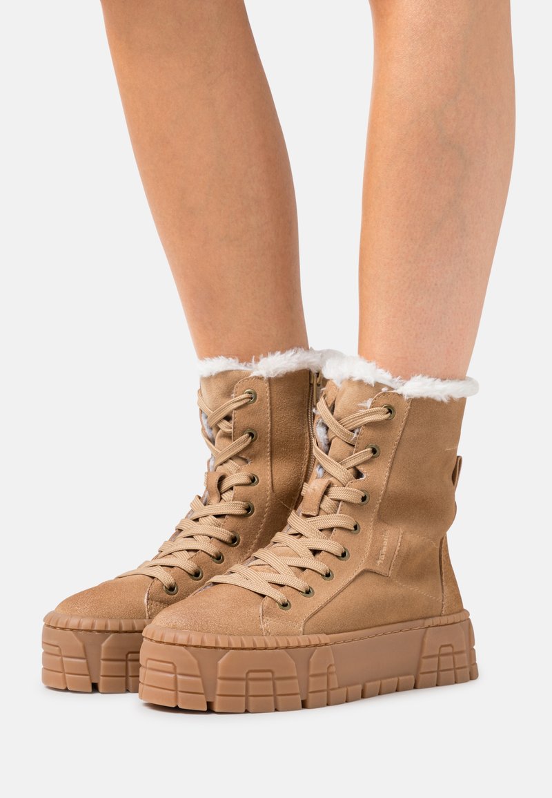 Hellbraune Ankle Boots aus Wildleder mit einem flauschigen weißen Kunstfellkragen, dicker Plateausohle und detailliertem Schnürverschluss.