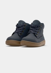 Botas de tobillo azul marino de cuero suave, con cordones redondos, ojales dorados y una suela de goma marrón para mayor agarre.