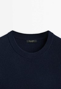 Tummansinisestä neulotusta villapuserosta, jossa on ribbitekstuuri, pyöreä kaula-aukko ja raglan-hihat. Lappu näkyvissä kaula-aukon sisäpuolella.