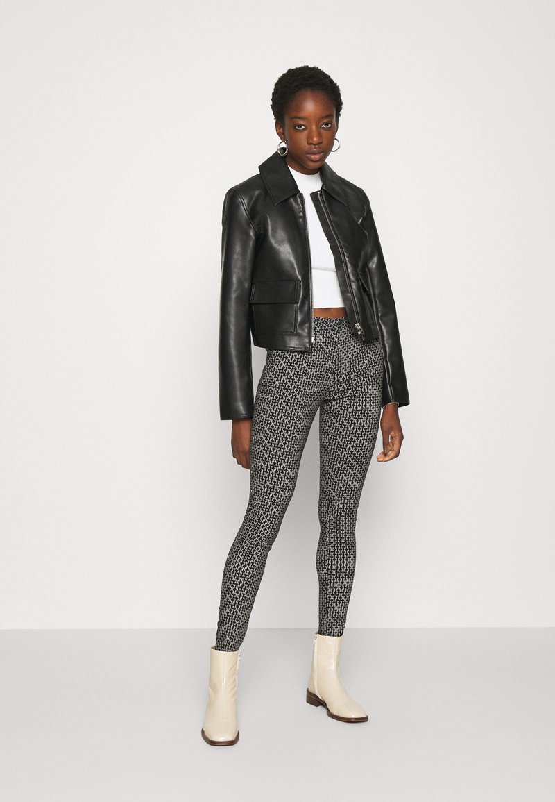 Veste en cuir noire courte, haut blanc ajusté, leggings à motifs noir et blanc, et bottines beiges à talon léger.
