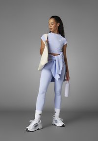 Svetlomodrý športový outfit, ktorý sa skladá z priliehavého topu a legín. Doplnky zahŕňajú svetlomodrý sveter viazaný okolo pása a krémovú kabelku cez rameno.
