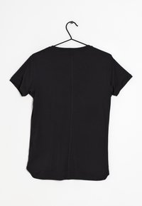 Una camiseta negra de manga corta colgada de un gancho negro. Presenta un cuello redondo y un dobladillo recto con un sutil detalle de costura en la parte posterior.