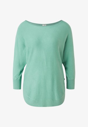 Miętowy, luźny sweter z zaokrąglonym dołem, zestawiony z podwiniętymi ciemnoszarymi dżinsami i kremowymi, wiązanymi botkami do kostki.