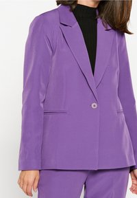Lila skräddarsydd kavaj i ett slätt tyg, med enkelknäppt stängning, notchade slag och sidfickor, kombinerad med en svart topp.