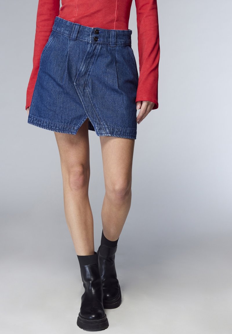 Gonna in denim con design a portafoglio, colore blu medio, pieghe nella parte anteriore, due bottoni neri in vita e cuciture a contrasto.
