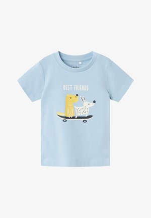 Camiseta de algodón azul claro con un gráfico de un perro amarillo y un conejo blanco con manchas sobre un monopatín, con el texto "MEJORES AMIGOS" encima.
