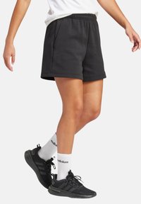 Pantalones cortos deportivos negros con una cinturilla elástica, bolsillos laterales y un ajuste relajado, combinados con zapatillas negras y calcetines blancos de marca.