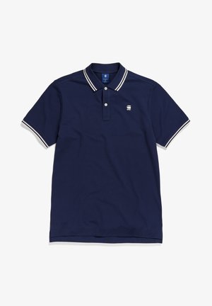 Polo de color azul marino hecho de algodón, con una tapeta de dos botones, mangas cortas y detalles a rayas blancas en el cuello y las mangas.