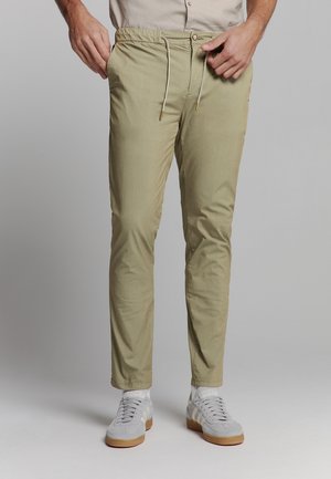 Khaki Stretchhosen mit einem Kordelzugbund, schmaler Passform und Taschen, kombiniert mit grauen Sportschuhen.