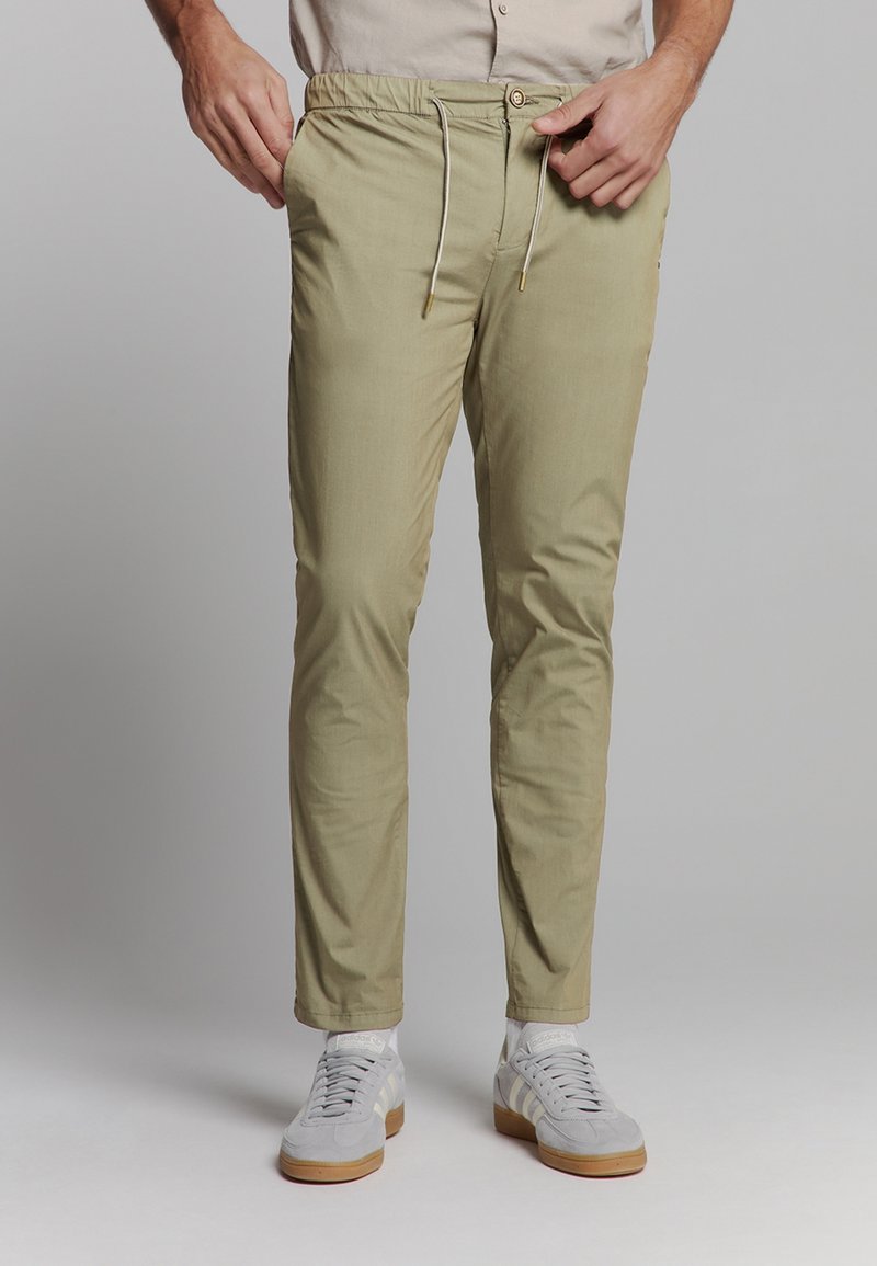 Khaki stretchbroek met een elastische taille, tapered fit en zakken, gecombineerd met grijze sportschoenen.