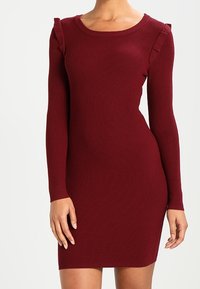 Abito in maglia a coste bordeaux con maniche lunghe, scollatura rotonda e dettagli arricciati sulle spalle. Design aderente e lunghezza al ginocchio.