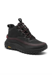 Chaussure de randonnée noire avec une tige texturée, des coutures d'accent rouge et une semelle Vibram robuste. Présente des oeillets renforcés et une boucle de traction à l'arrière.