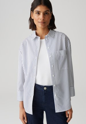 Witte shirt met marineblauwe verticale strepen, korte mouwen en een enkele borstzak, gecombineerd met donkerblauwe jeans. Gladde stofstructuur.