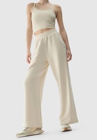 Beige Cropped-Top mit dünnen Trägern, kombiniert mit weiten, beigen Hosen. Glatter Stoff mit elastischem Taillenbund und kleinem Logo-Detail.