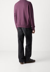 Fialová mikina s žebrovanými lemy na rukávech a spodním okraji, doplněná volnými tmavými džíny a černými teniskami s hnědými podrážkami.