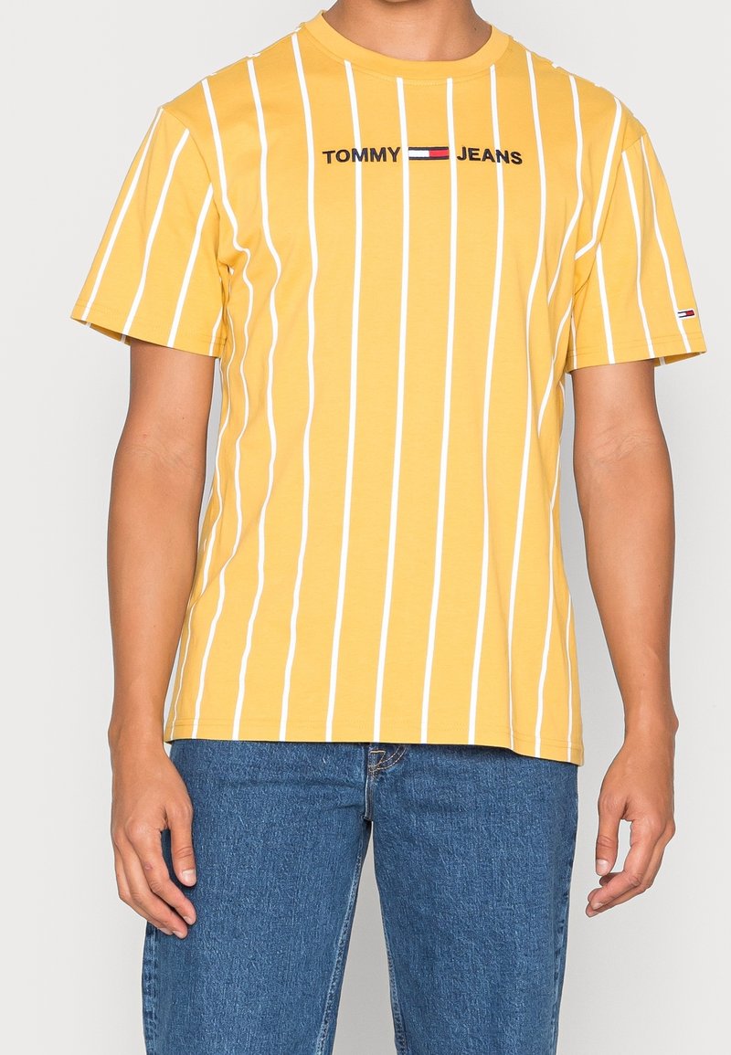 Yellow cotton t-shirt with white vertical stripes, featuring black "TOMMY JEANS" text logo at the chest and a small logo detail on the sleeve.