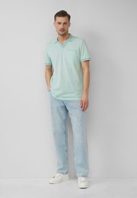 Lichtgroene poloshirt met V-hals en zak, voorzien van een contrasterende kraag en mouwt trims. Gecombineerd met lichtblauwe jeans en witte sneakers.
