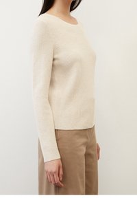 Pull en maille beige clair à manches longues, col rond, texture côtelée et coupe droite à la taille. Associé à un pantalon beige clair.