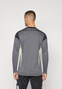 Langmouw sportshirt in grijs met zwarte accenten en limegroene zijpanelen, gemaakt van lichtgewicht vochtafvoerend materiaal, met een gladde textuur.
