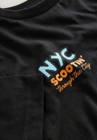 Schwarzes Baumwoll-T-Shirt mit bedrucktem Text: "NYC SCOOTIN' durch die Stadt" in Blau, Orange und Weiß, mit Rundhalsausschnitt und Taschen-Detail.