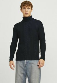Pull à col roulé bleu marine en tissu tricoté textur�é, avec un motif de torsades et des poignets et un ourlet côtelés, associé à un jean en denim clair.