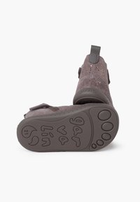 Scarpe in suede marrone con strap a velcro, dotate di una suola in gomma testurizzata con motivi e dettagli in rilievo, progettate per bambini.