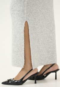 Robe en tricot côtelé gris avec détail de fente sur le côté, associée à des escarpins à talons aiguilles noirs avec un petit accent de boucle.