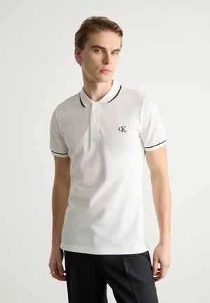 Weißes Baumwoll-Polohemd mit schwarzen Akzenten am Kragen und an den Ärmeln, mit einem kleinen gestickten Logo auf der Brust.