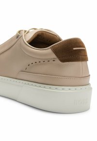 Light beige leather sneaker with a brown suede heel accent, white rubber sole, and decorative stitching on the upper. Branding on the heel.
