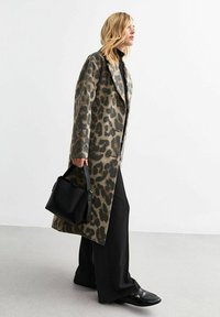 Leopardprint wollen jas met een getailleerde pasvorm, brede revers en gestructureerde stof. Gecombineerd met losse zwarte broek en een kleine zwarte handtas.