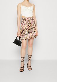 Vit kortärmad topp med knyt fram, parat med en färgglad minikjol med blommönster i rosa, bruna och gyllene toner. Svarta sandaletter med remmar och handväska.