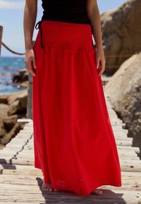 Gonna maxi rossa fluente con vita smock, realizzata in tessuto leggero, caratterizzata da una vestibilità comoda e un design fino alla caviglia.