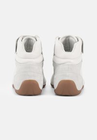 Vit och ljusgrå sneaker med överdel i mocka och läder, vadderad krage, kardborrband och sula i gummigummi; designad för stöd.