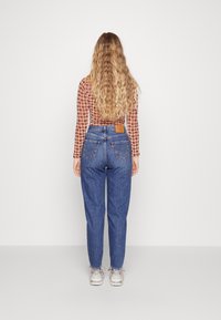 Jeansy w kolorze niebieskim o wysokim stanem, w luźnym kroju, z brązową skórzaną metką z tyłu, oraz fakturowana bluzka z długim rękawem w wzór.