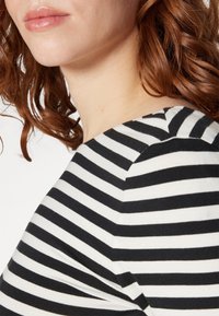 Randig topp i svart och vitt med rund halsringning och mjukt tyg, framhäver sömsdetaljerna och den mjuka draperingen längs axeln.