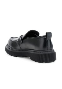 Mocasín negro de cuero con suela gruesa acanalada, detalles de costura y lengüeta trasera, en ángulo para mostrar la vista lateral y trasera.