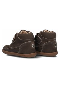 Braune Lederstiefeletten mit einer weichen Fütterung, Klettverschluss und Gummisohlen, die mit kontrastierendem Näht und einem runden Akzent auf der Rückseite versehen sind.