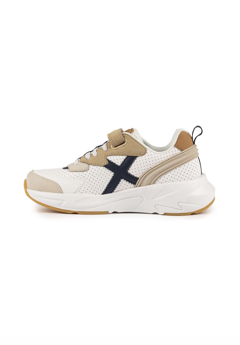 Sneaker blanc et beige avec cuir perforé, accents navy et semelle épaisse. Comprend des lacets et une languette au talon.