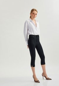 Pantalones recortados negros con un diseño ajustado, que cuentan con bolsillos laterales y detalles de dobladillo partido, combinados con una camisa blanca de botones y tacones de estampado de leopardo.
