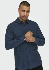 Mørkeblå skjorte med knapper, lavet af tekstureret stof, med en brystlomme og knapmanchetter. Slim fit med en rundet søm.