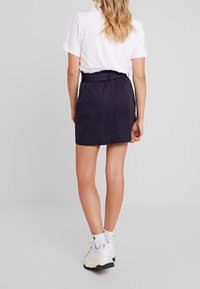 Gonna blu navy con vita a cintura, realizzata in tessuto dalla texture liscia. Il design è tailoring e arriva fino al ginocchio. T-shirt bianca e sneakers.