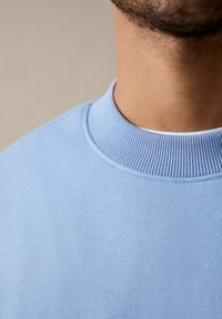 Lichtblauwe sweatshirt met een geribde ronde hals. De stof lijkt zacht en gestructureerd, met een eenvoudig ontwerp zonder zichtbare patronen.