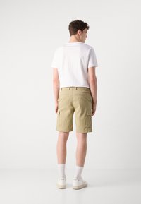 Beige cargo shorts made of cotton with side pockets and back flap pockets, paired with a plain white T-shirt and white sneakers.