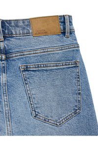 Poche arrière d’un jean en denim bleu clair avec des surpiqûres orange et un patch en cuir marron portant la marque Vero Moda We Do Denim.