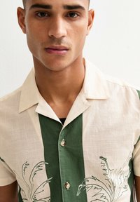Camicia a maniche corte in lino, con strisce crema e verde scuro e illustrazioni di piante. Design con bottoni e dettagli in perla.