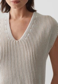 Haut en maille à col en V blanc et beige, avec côtes verticales et manches courtes. Tissu doux et texturé avec un motif à tissage ouvert.