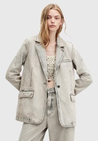 Blazer in denim grigio chiaro con rever a punta, due tasche frontali e cuciture a contrasto. Abbinato a un top cropped testurizzato e pantaloni coordinati.